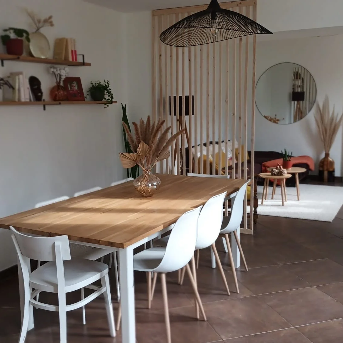 Salle à manger avec une table en bois, chaises blanches, décoration intérieure moderne, diviseur en bois, salon avec canapé, table basse, miroir rond sur le mur, plantes