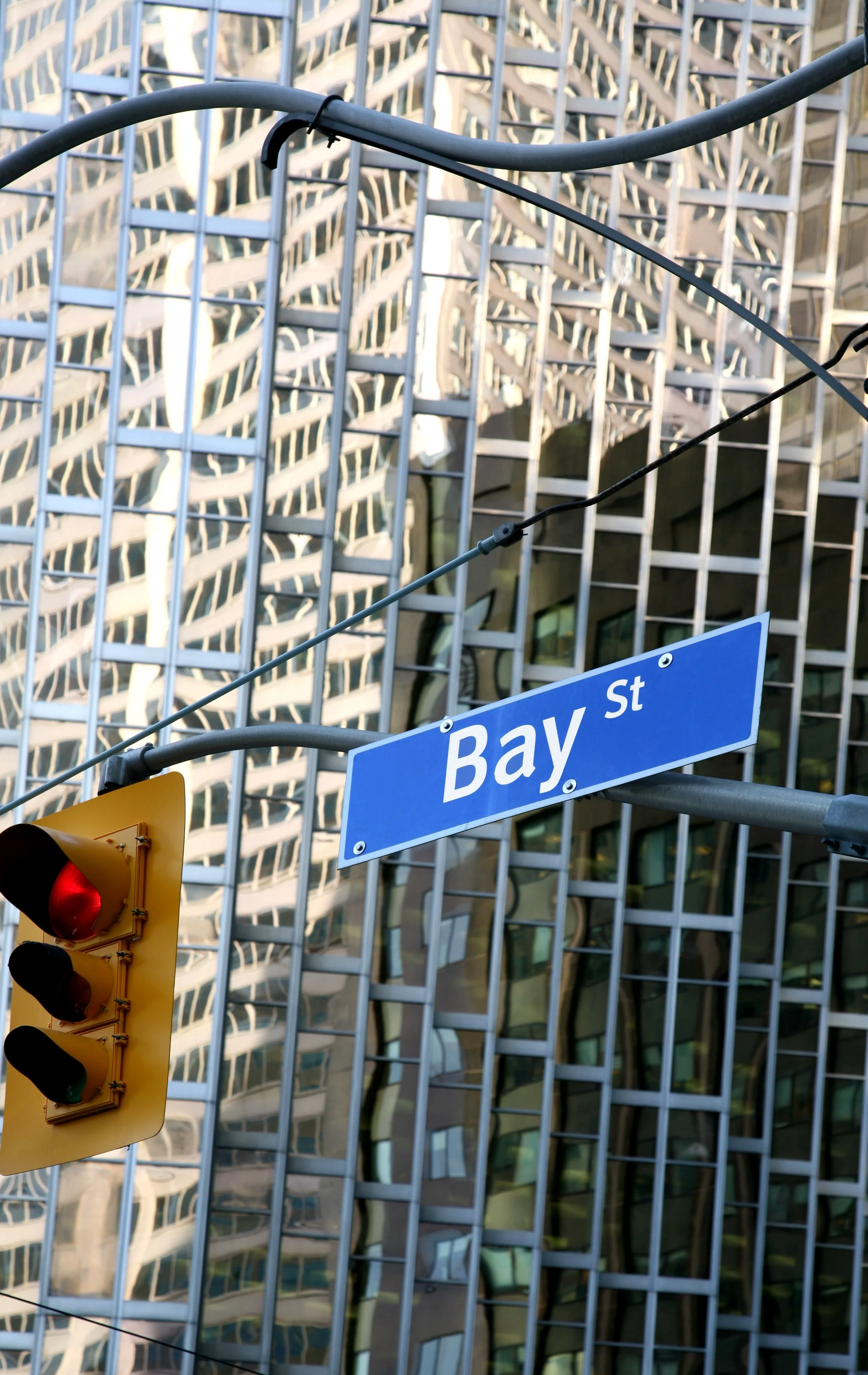 A street sign for Bay Street, a traffic light showing red, and a modern glass building with a distinctive grid pattern in the background.