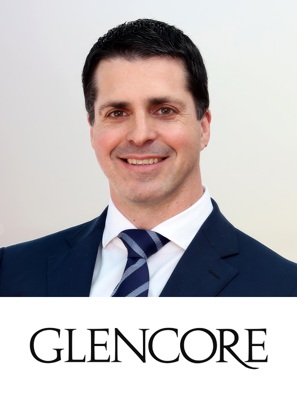 A smiling man in a dark blue suit, white shirt, and striped tie, with the word 'GLENCORE' written below him in bold black letters.