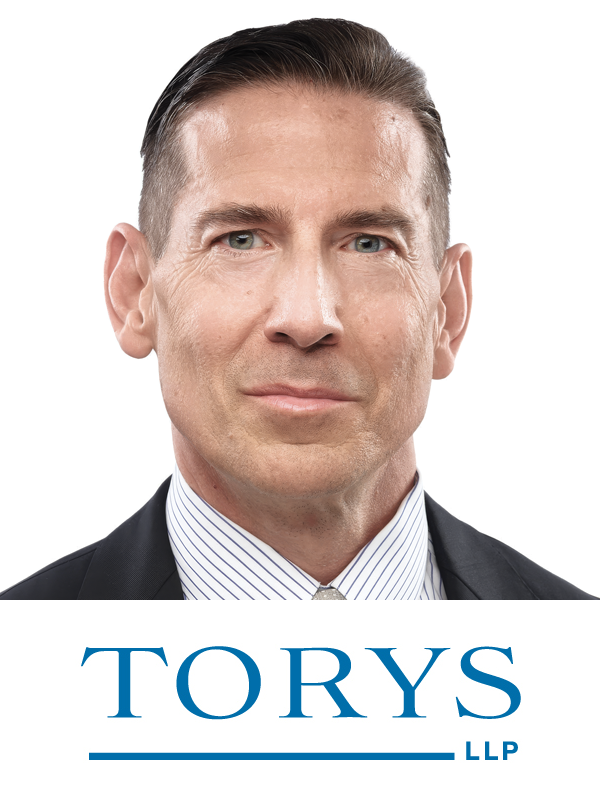Professional portrait of a middle-aged man with short dark hair, wearing a suit and tie, against a white background with the TORYS LLP logo.