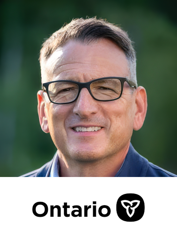 A man with glasses smiling outdoors with a blurred green background, and the Ontario logo and text at the bottom.