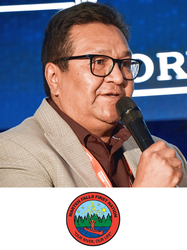 A man in glasses and a beige blazer speaking into a microphone at an event.
