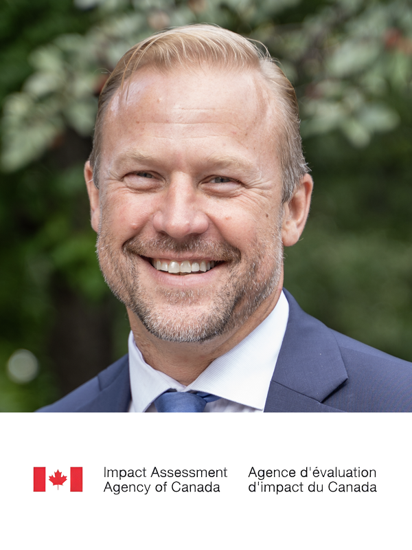 Smiling man in a blue suit and tie outside with greenery in the background. Logo of the Agency of Canada and Impact Assessment displayed at the bottom.