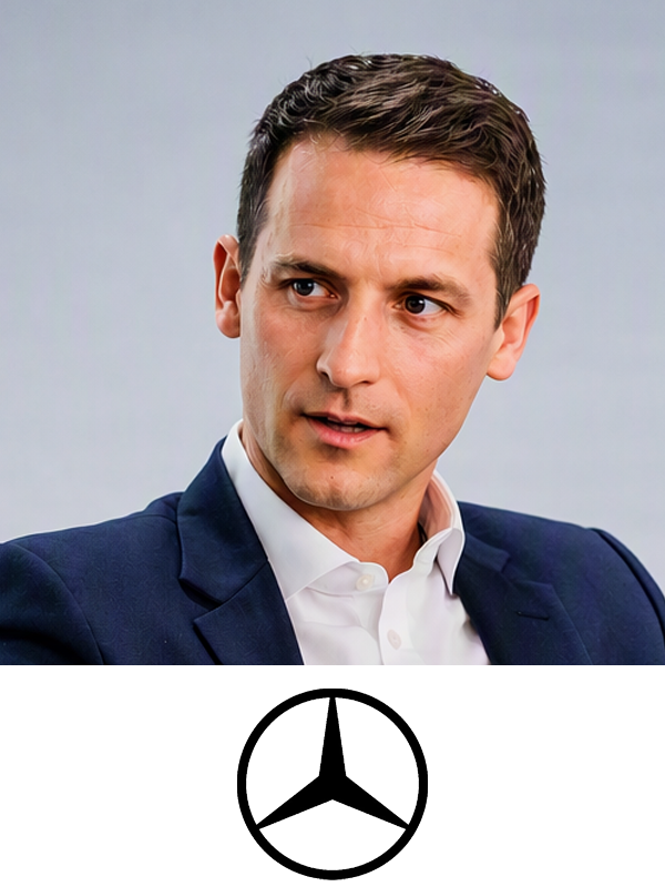 A man in a dark suit and white shirt looks to his left with a serious expression, against a plain background with a Mercedes-Benz logo below