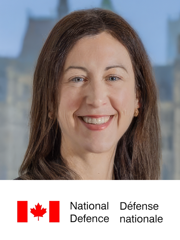 A smiling woman with long brown hair in front of a blurred building background, with the Canadian flag and text 'National Defence' and 'Défense nationale' at the bottom.