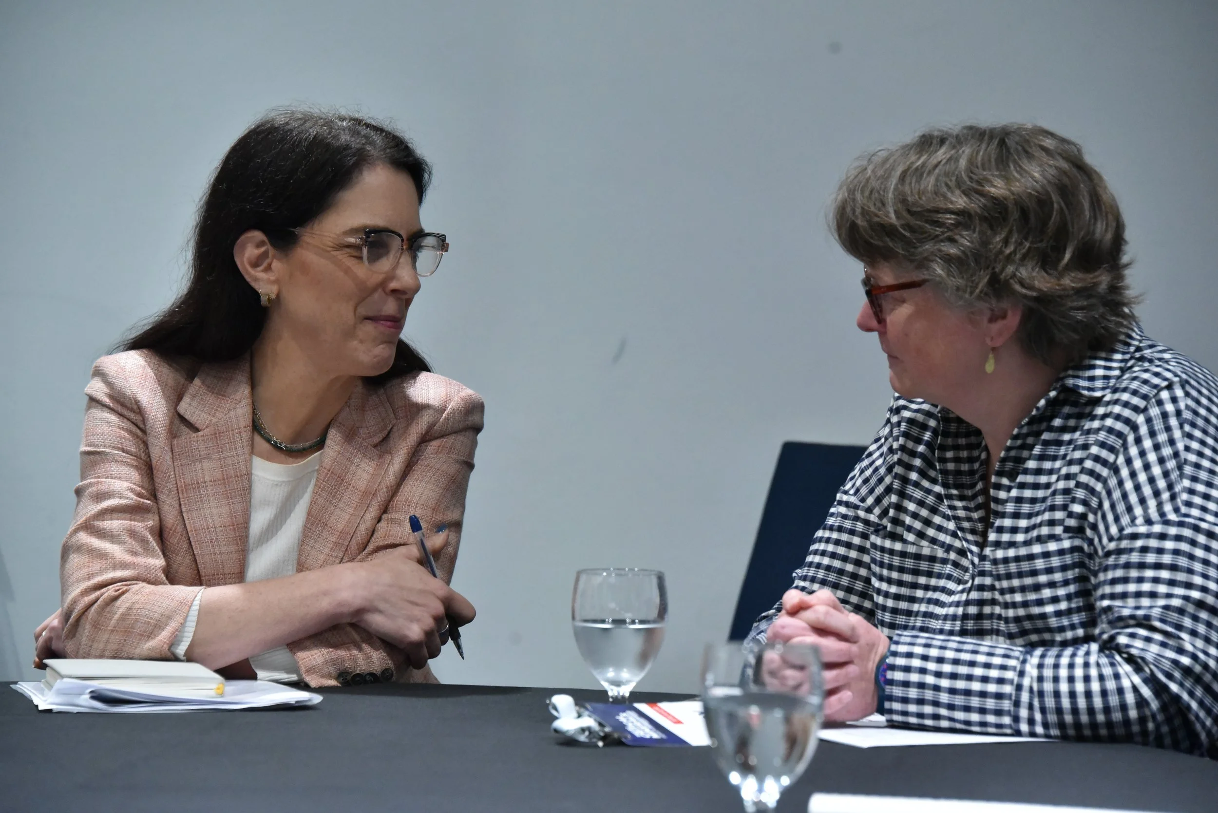 Two women engaged in conversation at a table with notebooks and glasses of water.