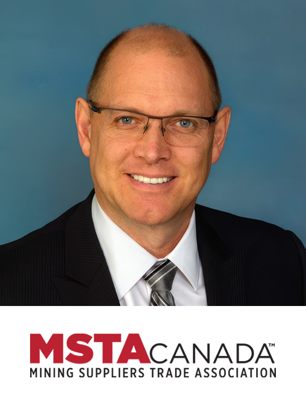 A professional portrait of a smiling man wearing glasses, a dark suit, white shirt, and a striped tie, with a blue background. The lower part of the image displays the logo for MSTA Canada - Mining Suppliers Trade Association.