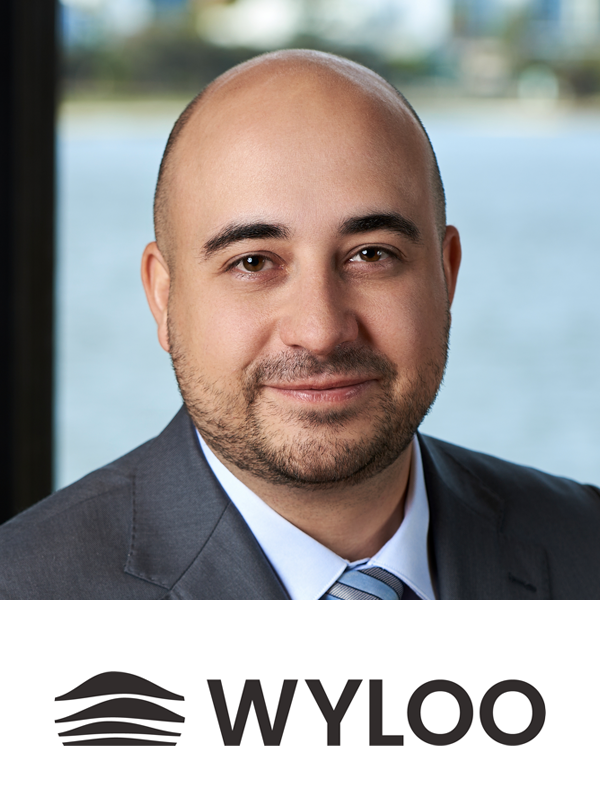 A man in a business suit with a water view and trees in the background, and the WYLOO logo below.