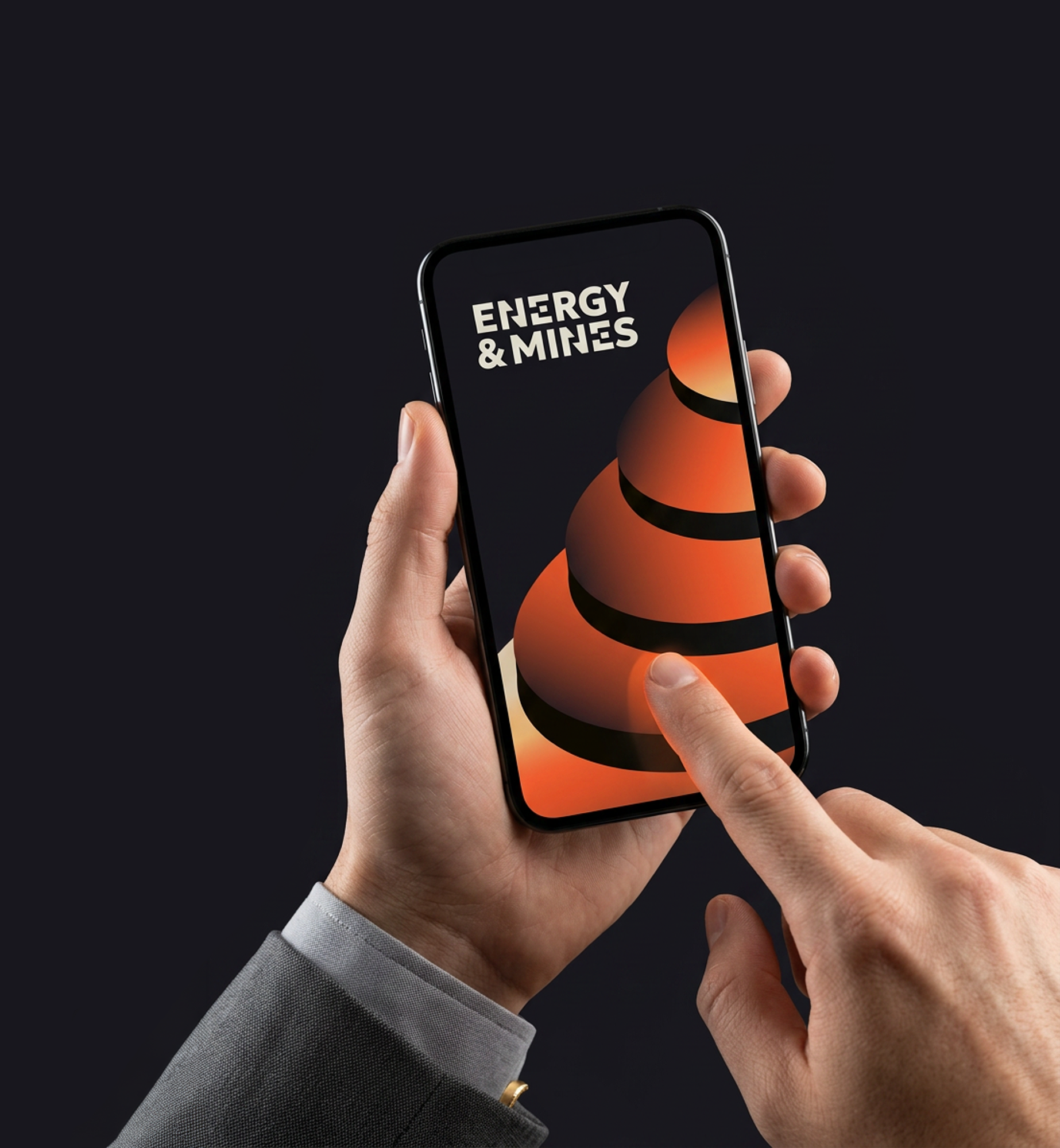 Close-up of a person holding a smartphone with a dark background. The phone screen displays the words 'ENERGY & MINES'. The person is wearing a gray suit and has a gold ring on one finger.