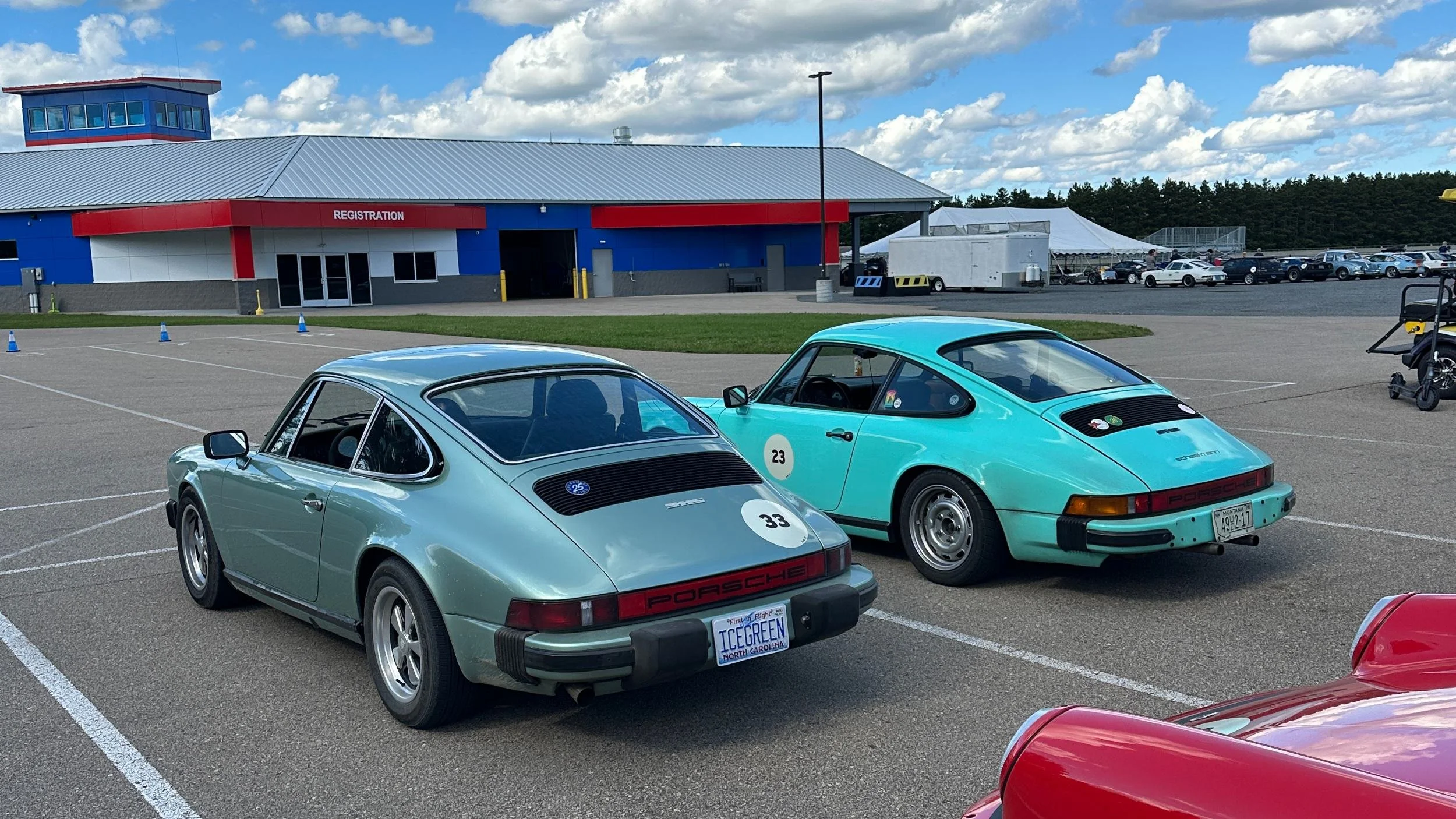 Two 1970s Porsche 911s parked side by side at the Overcrest Rally registration building, one ice green metallic with North Carolina plates and one mint with Montana plates