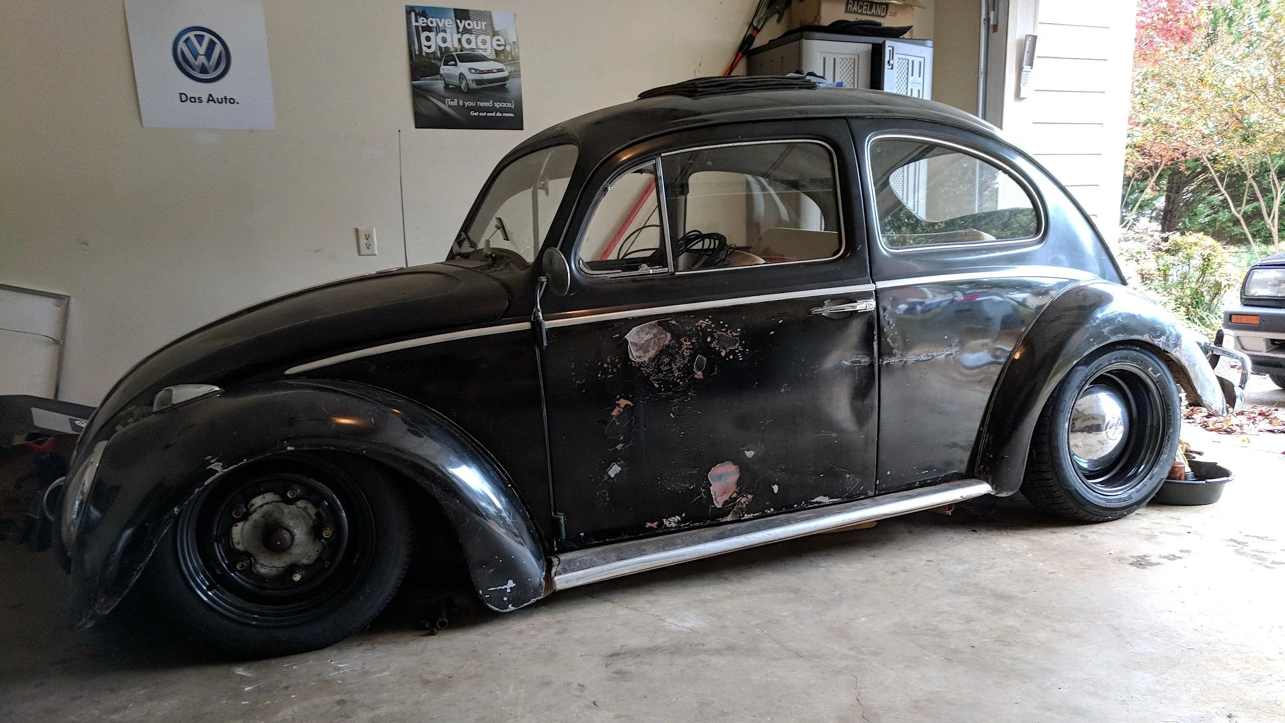 Black 1961 Volkswagen Beetle sitting low in a home garage with bare filler patches on both doors