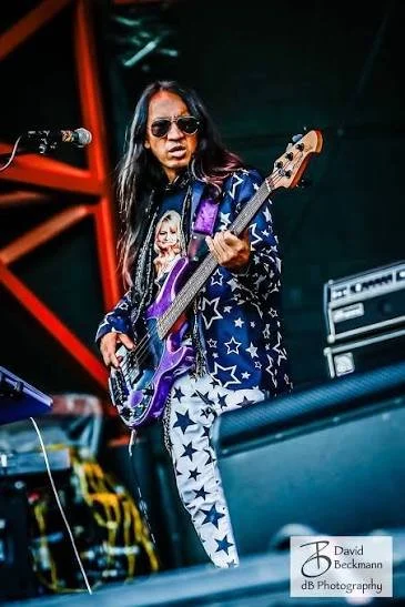 A woman wearing sunglasses and a star-patterned jacket playing an electric guitar on stage at a music performance.