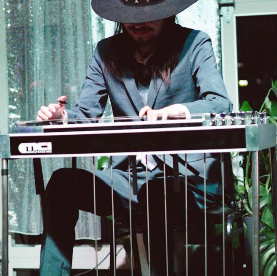 A person wearing a dark wide-brimmed hat and dark clothing playing a vibraphone.