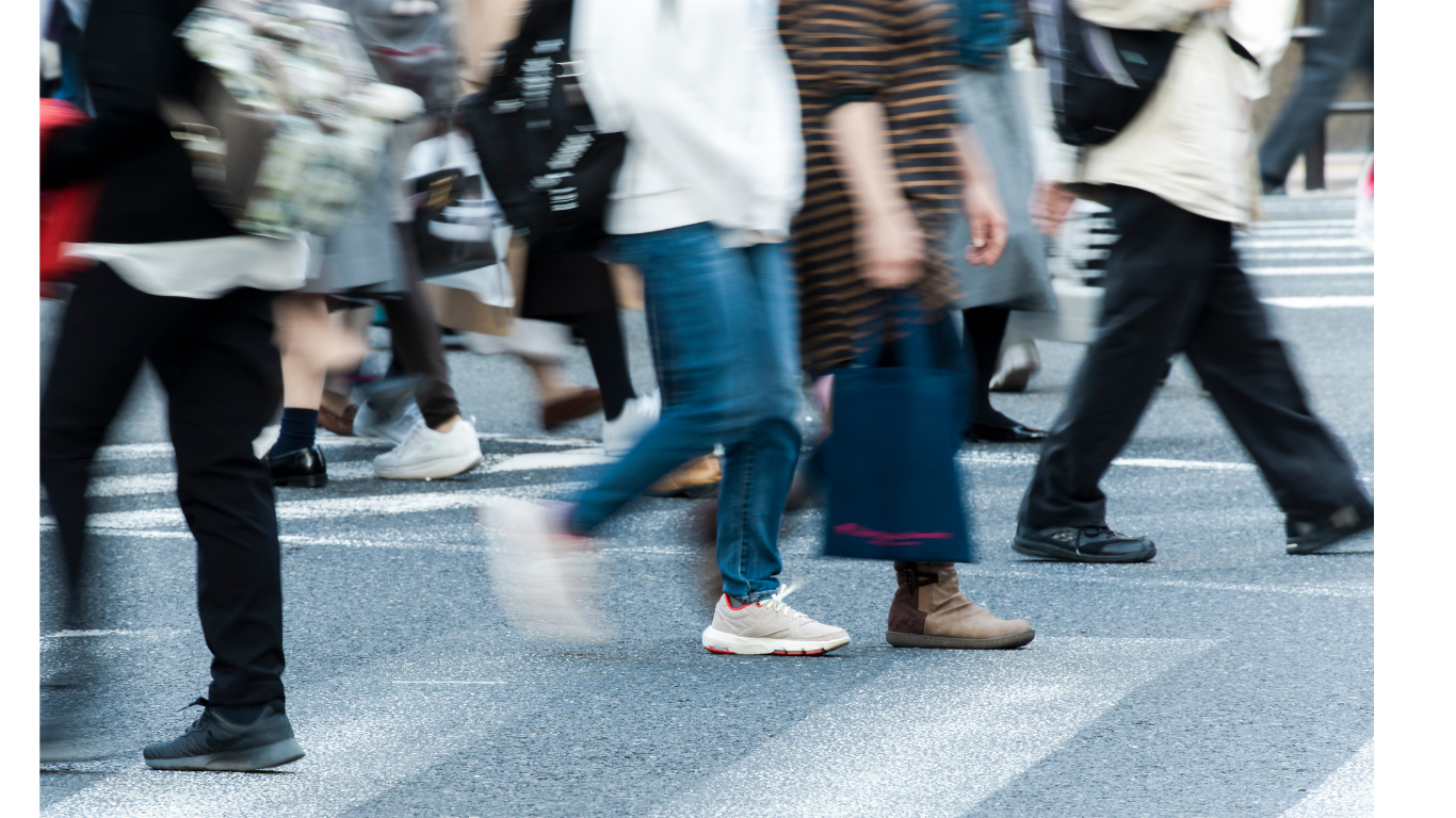 People walking across a city street crosswalk, some carrying shopping bags, dressed in casual clothing.