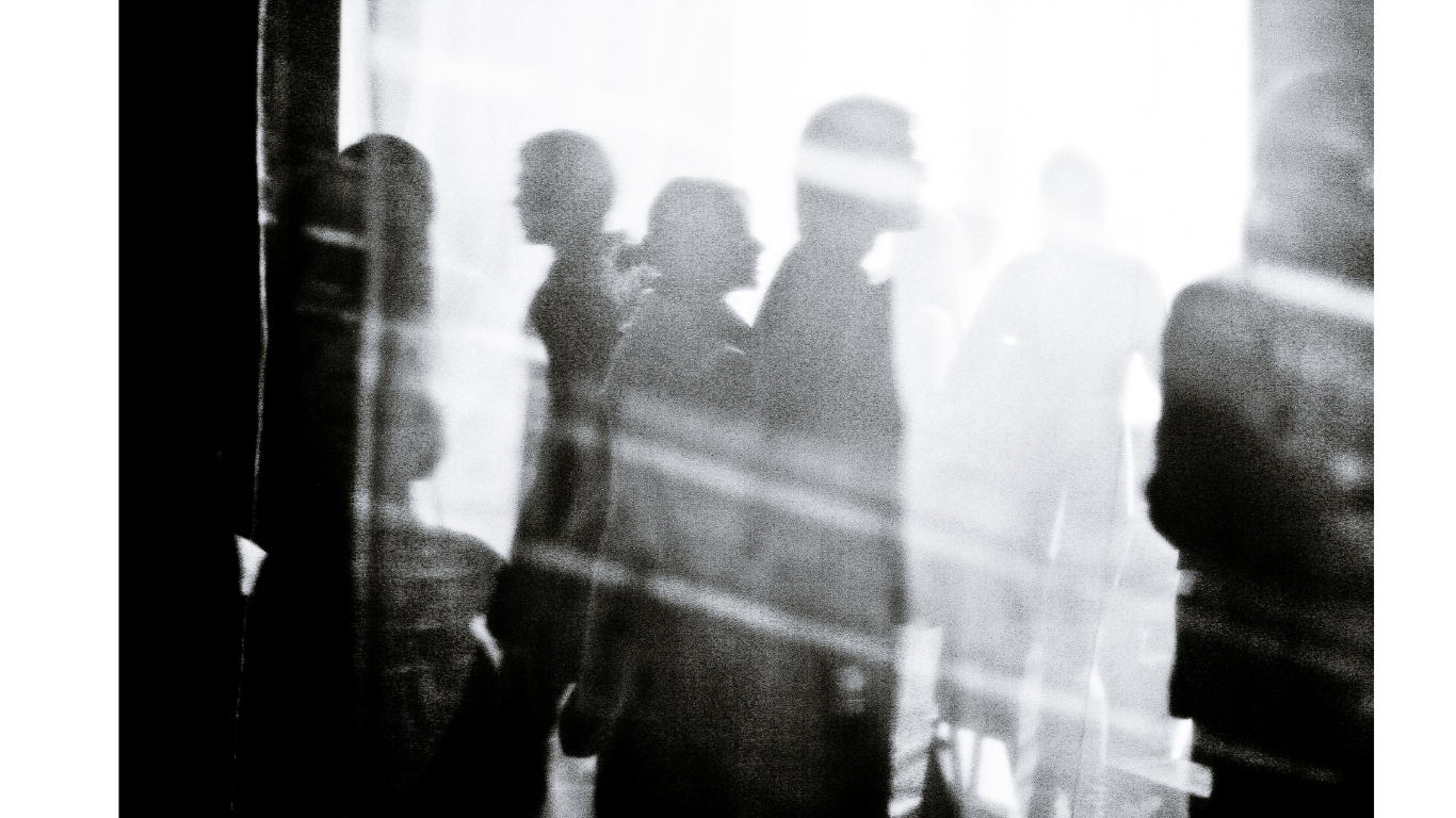 Silhouettes of people walking past a glass window with sunlight shining through.