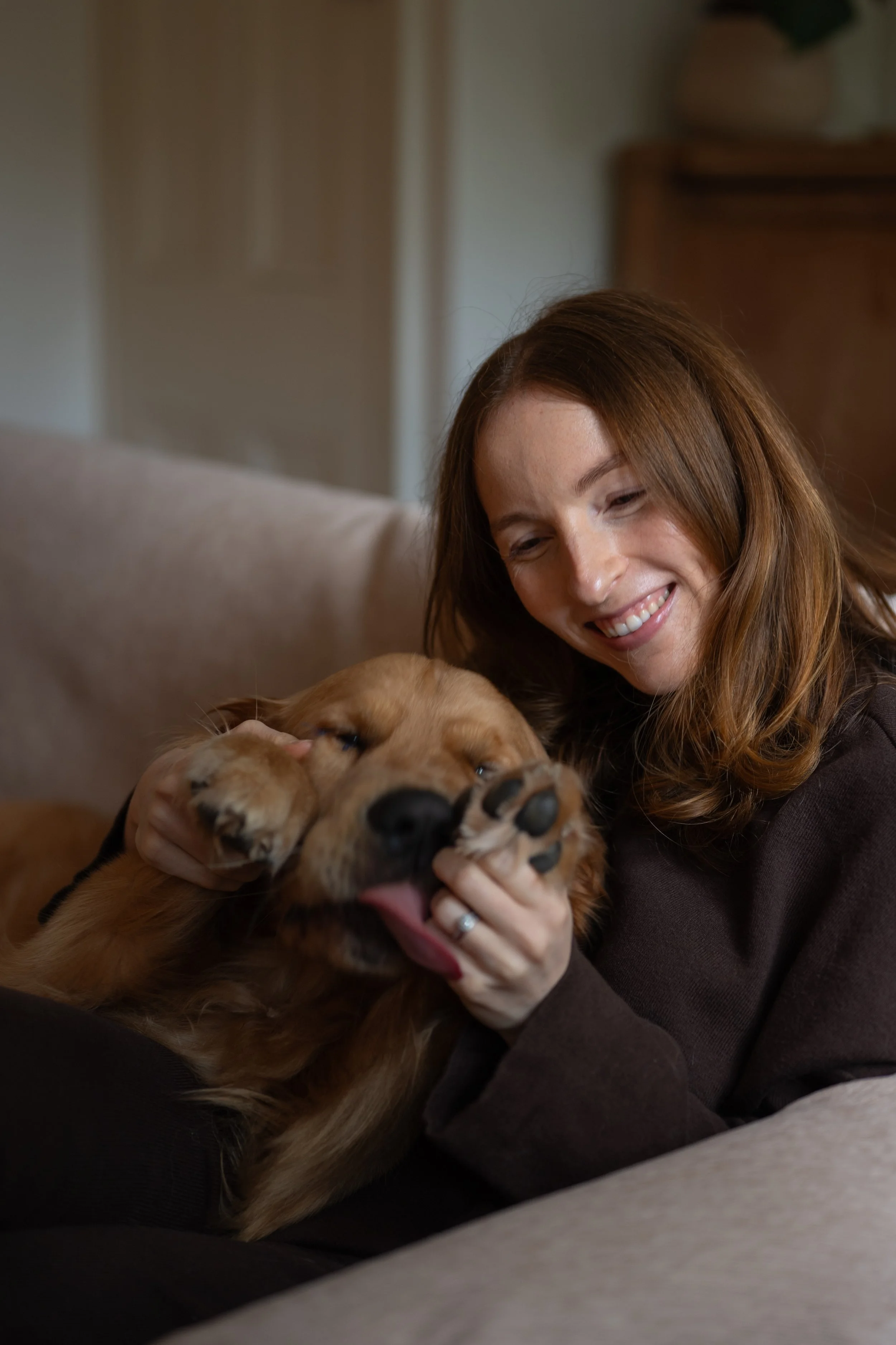 A woman with long brown hair smiling and holding a large brown dog that is lying on its back with paws up.