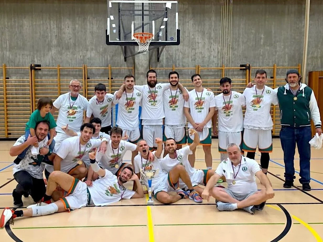 Un gruppo di giocatori di basket che festeggiano una vittoria in una palestra, con medaglie e un trofeo.