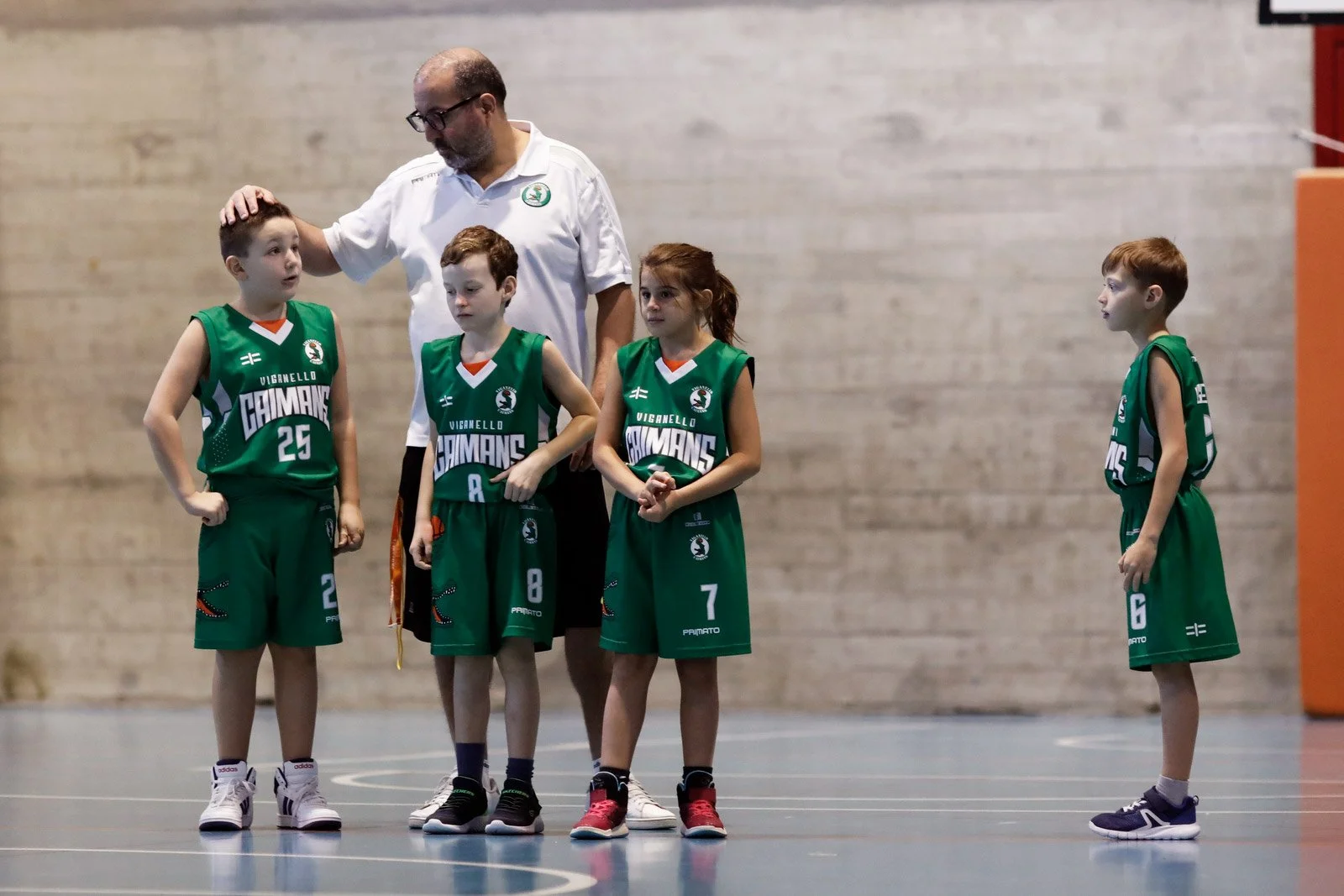 Un allenatore di basket con quattro giovani giocatrici in divisa verde, all'interno di una palestra