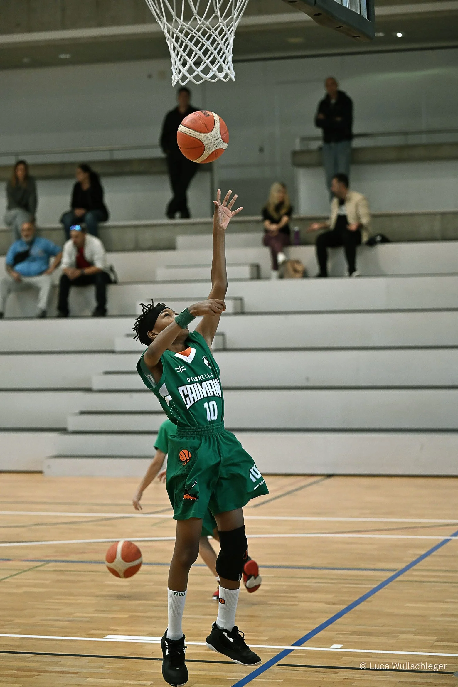 Giocatrice di pallacanestro in azione durante una partita, che si sta preparando a lanciare il pallone verso il canestro, all'interno di un impianto sportivo, con spettatori sullo sfondo.
