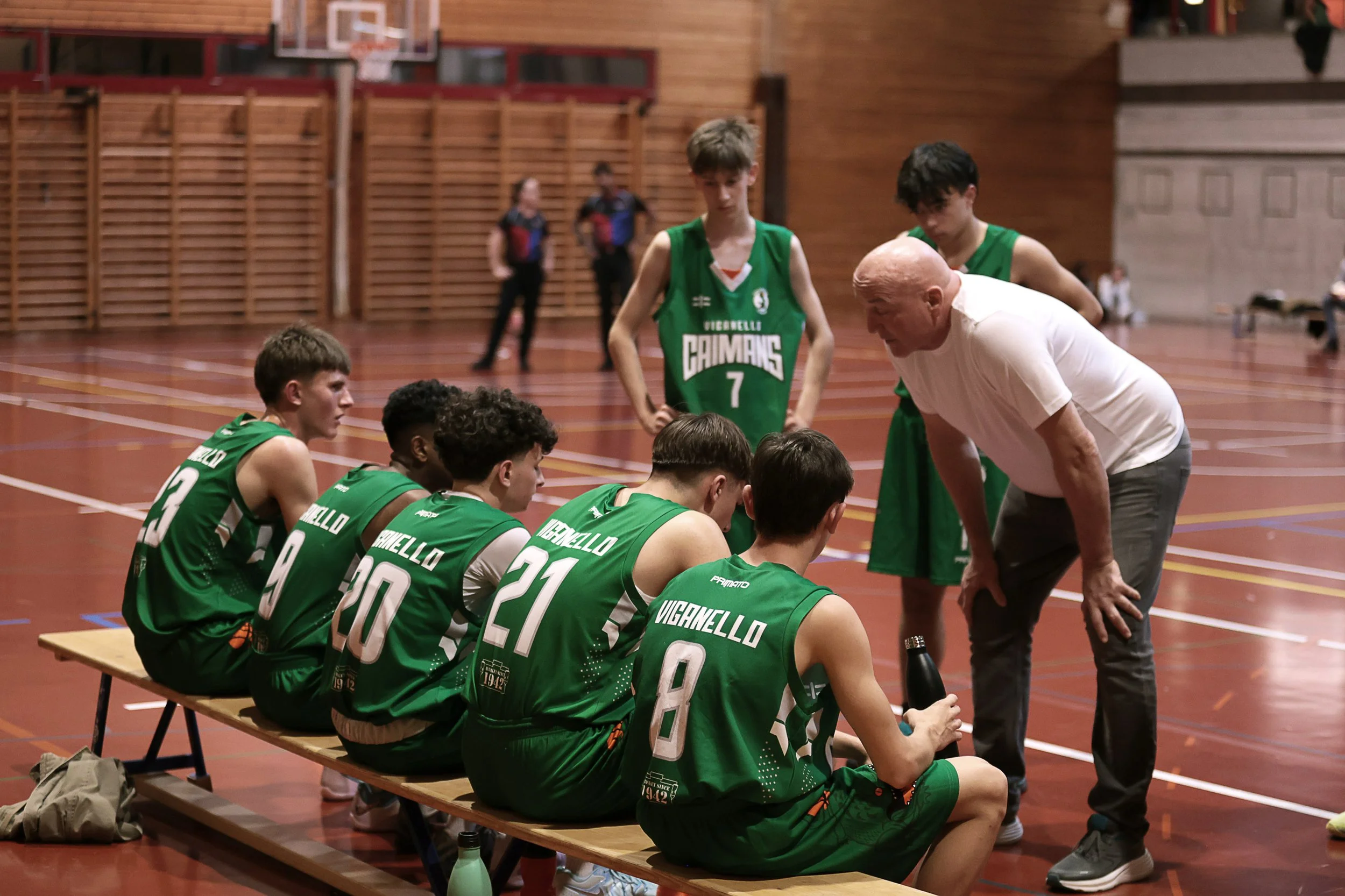 Una squadra di basket militare seduta in panchina durante una partita, con un loro allenatore che dà istruzioni.