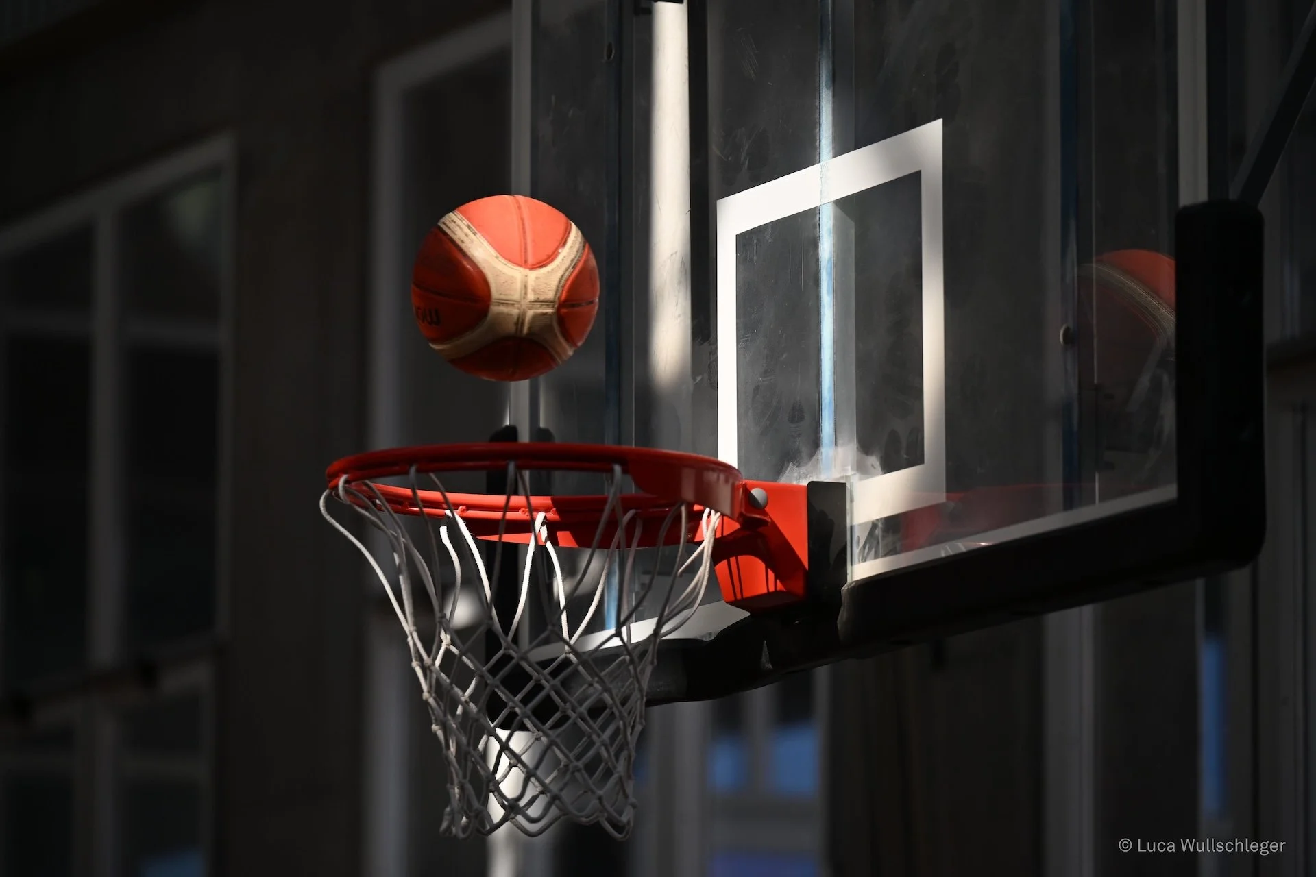 Pallone da basket arancione che entra nel canestro di una tabella da basket in un'arena sportiva.