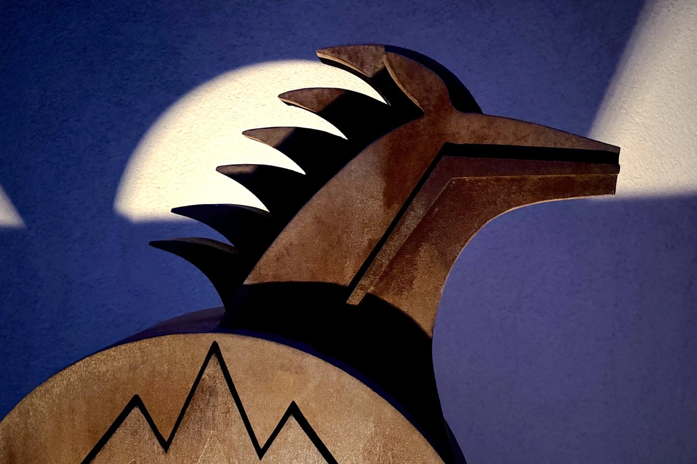 Close-up of a wooden lamp with carved design, casting a shadow on a textured wall.