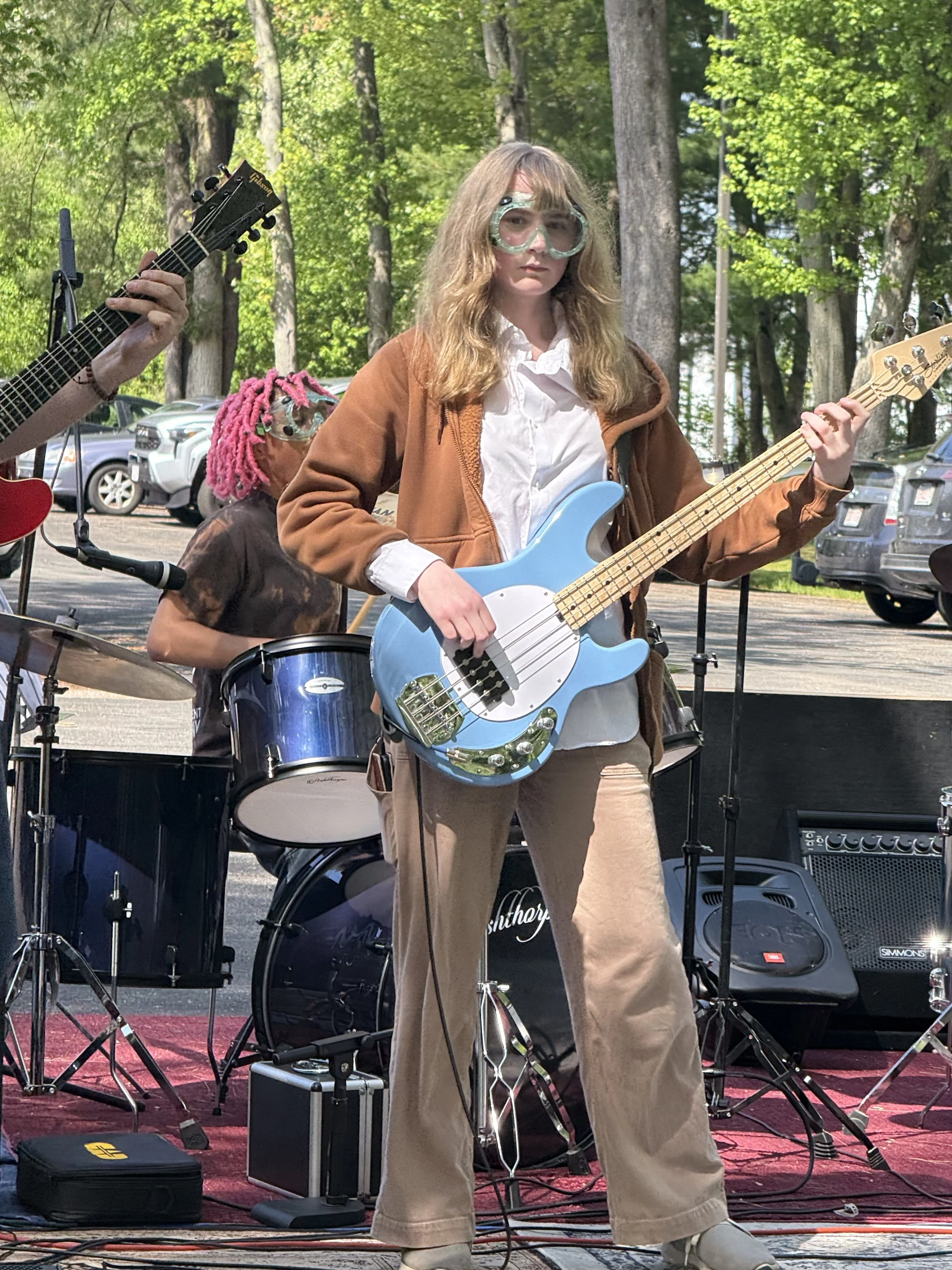 Tremont School students performing live music outdoors, with a bassist and drummer on stage.