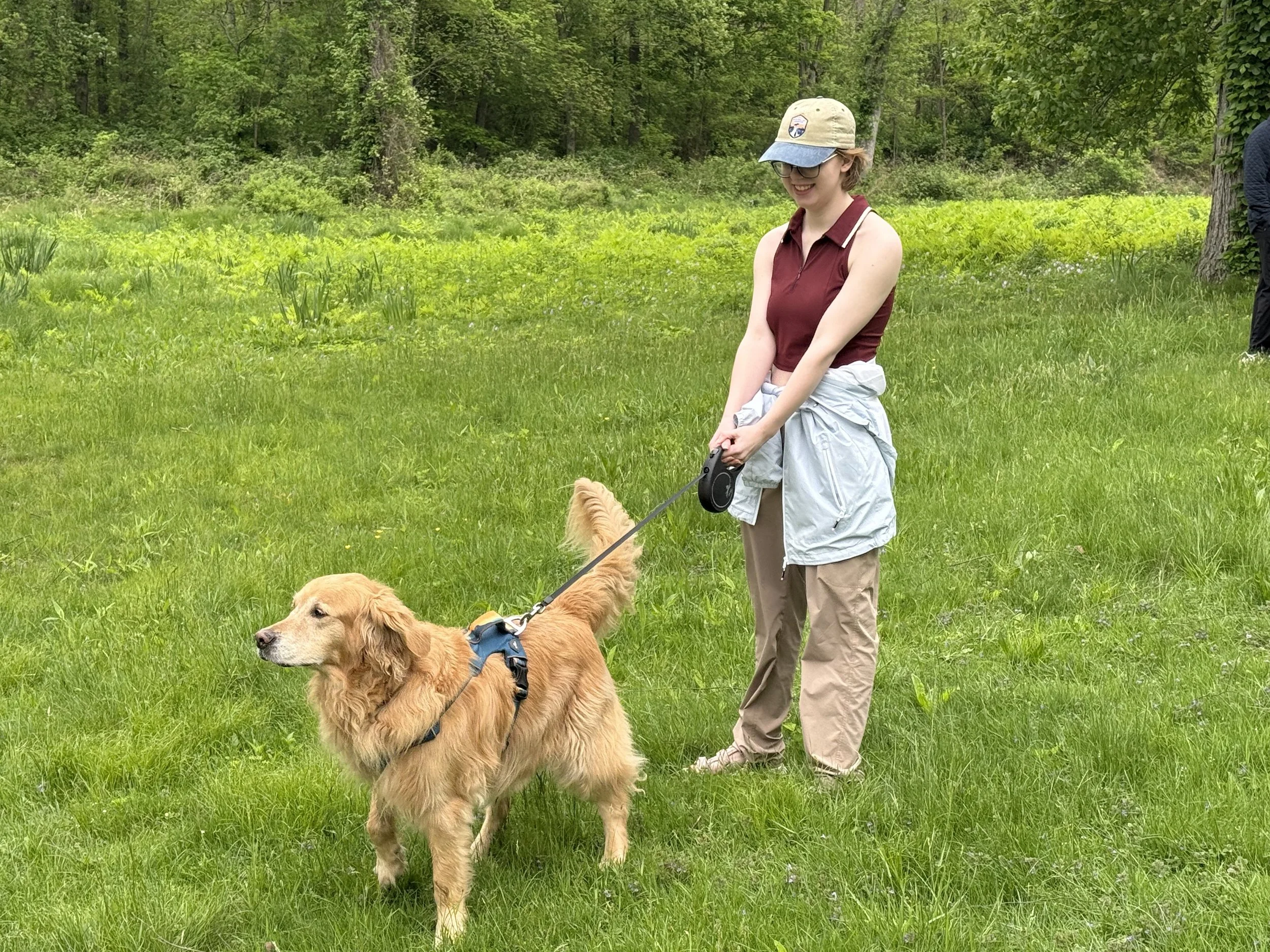 A Tremont School student walks a golden retriever through a grassy field on an outdoor community outing.