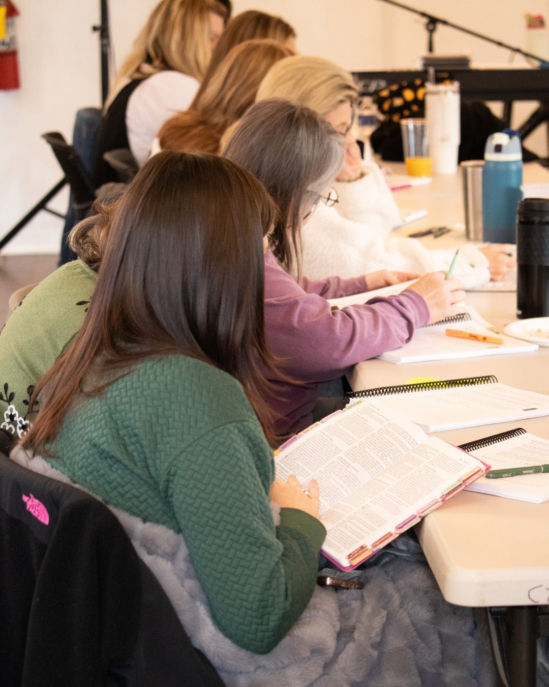 Women sitting at a table attending a seminar or workshop, reading notebooks and textbooks.
