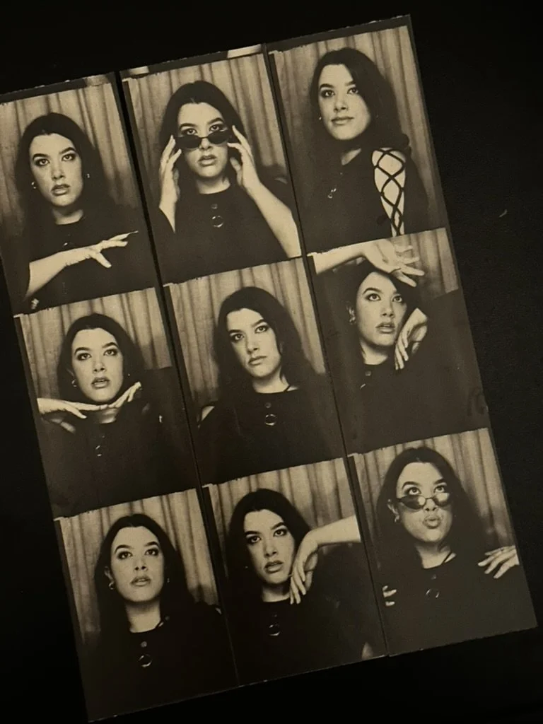 Strip of black and white photo booth images featuring a woman with dark hair in various poses, including adjusting sunglasses, touching her face, and looking at the camera.