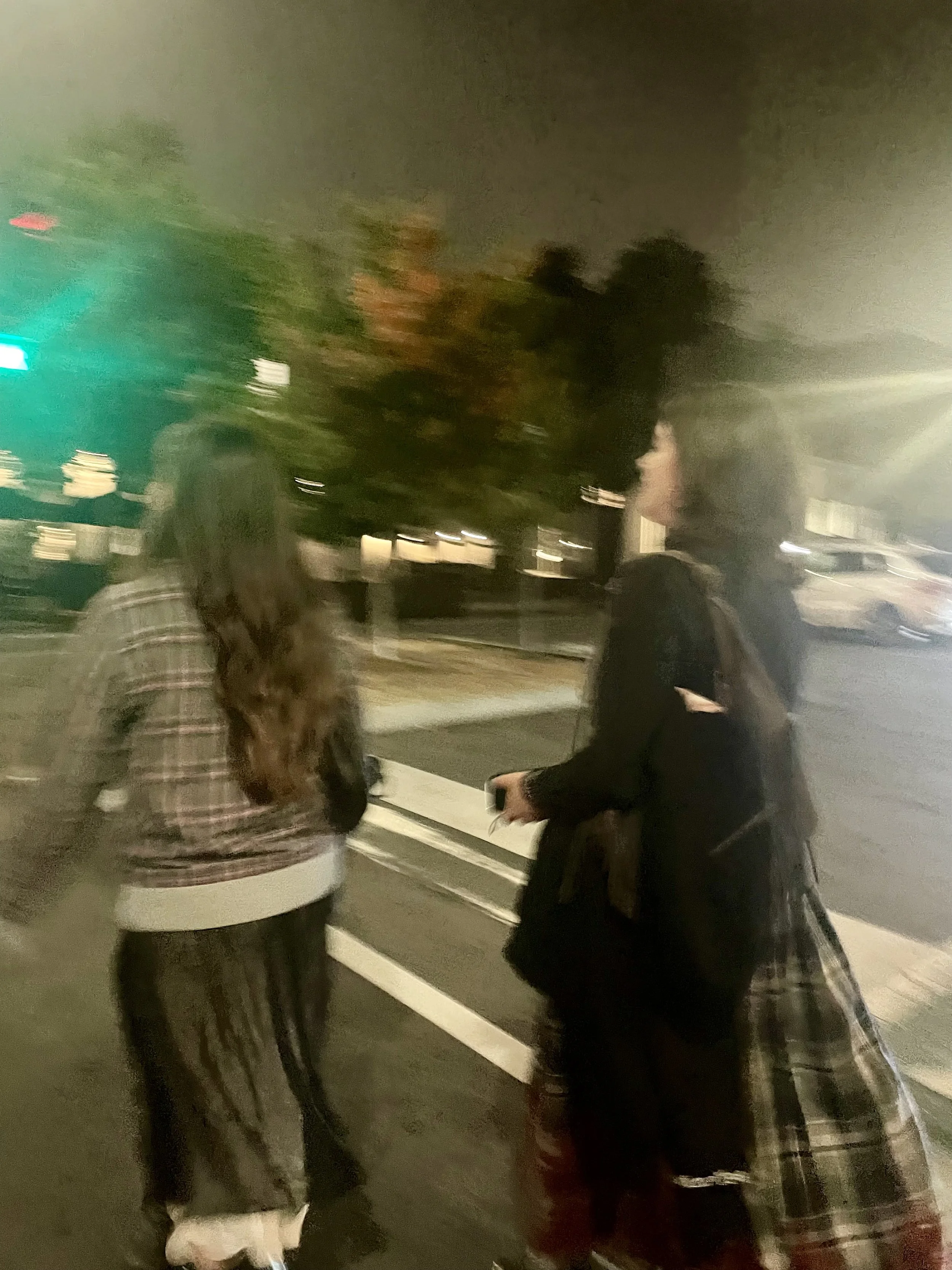 Nighttime street scene with three people and cars, cloudy sky, and trees.
