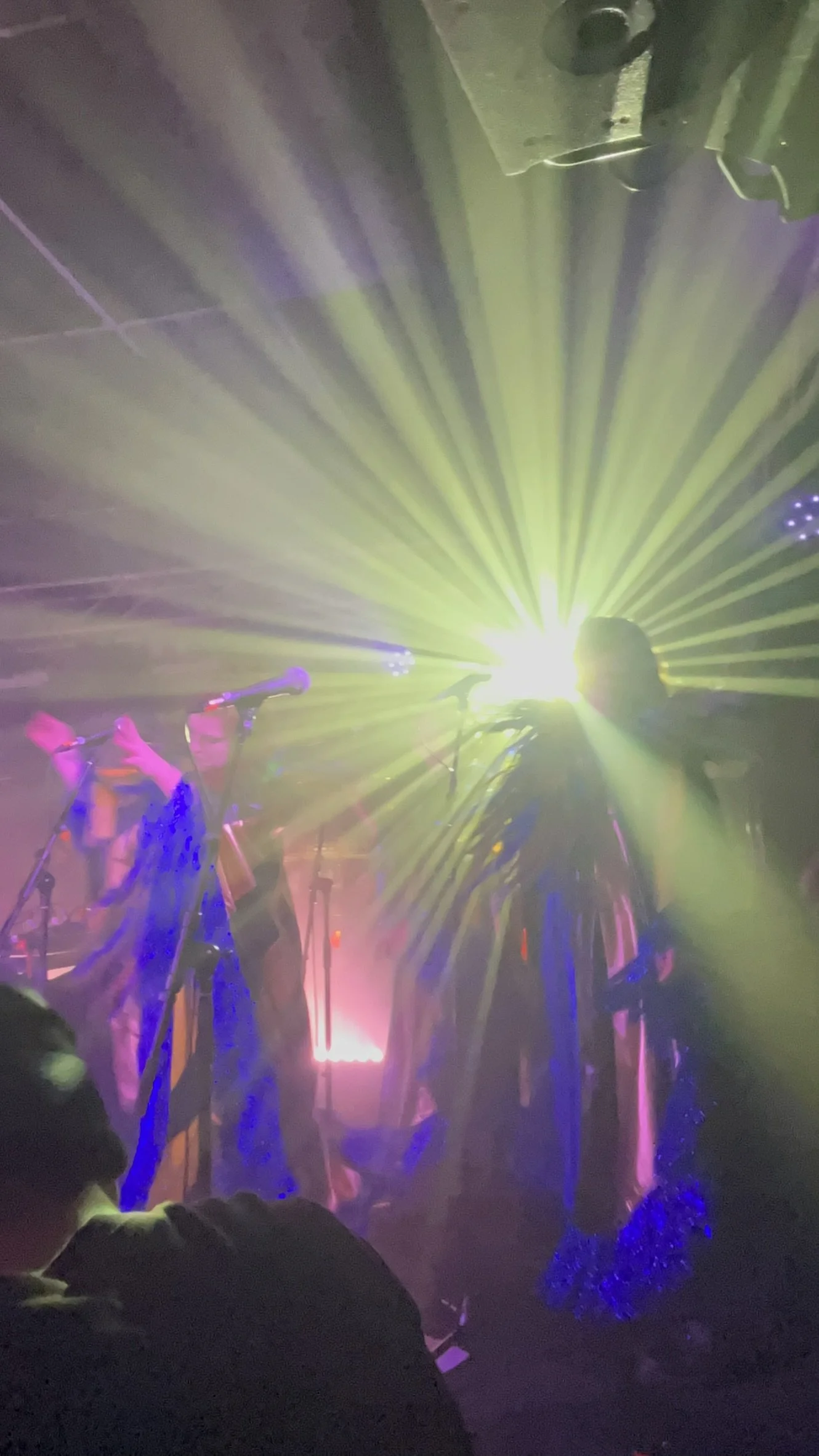 A stage with bright, colorful lights and people standing in front. The scene appears to be at a concert or live performance.