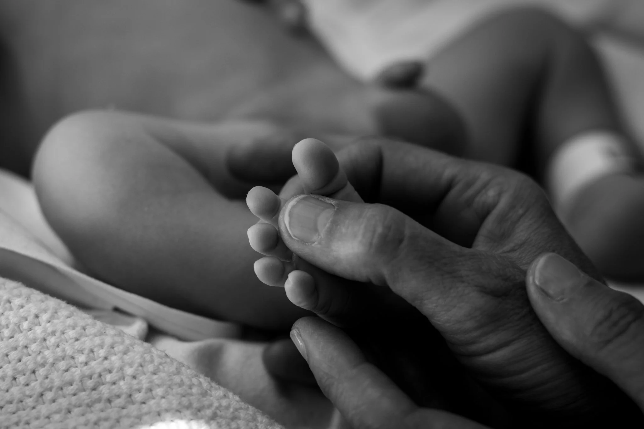 A person holding a baby's foot with both hands, in black and white.