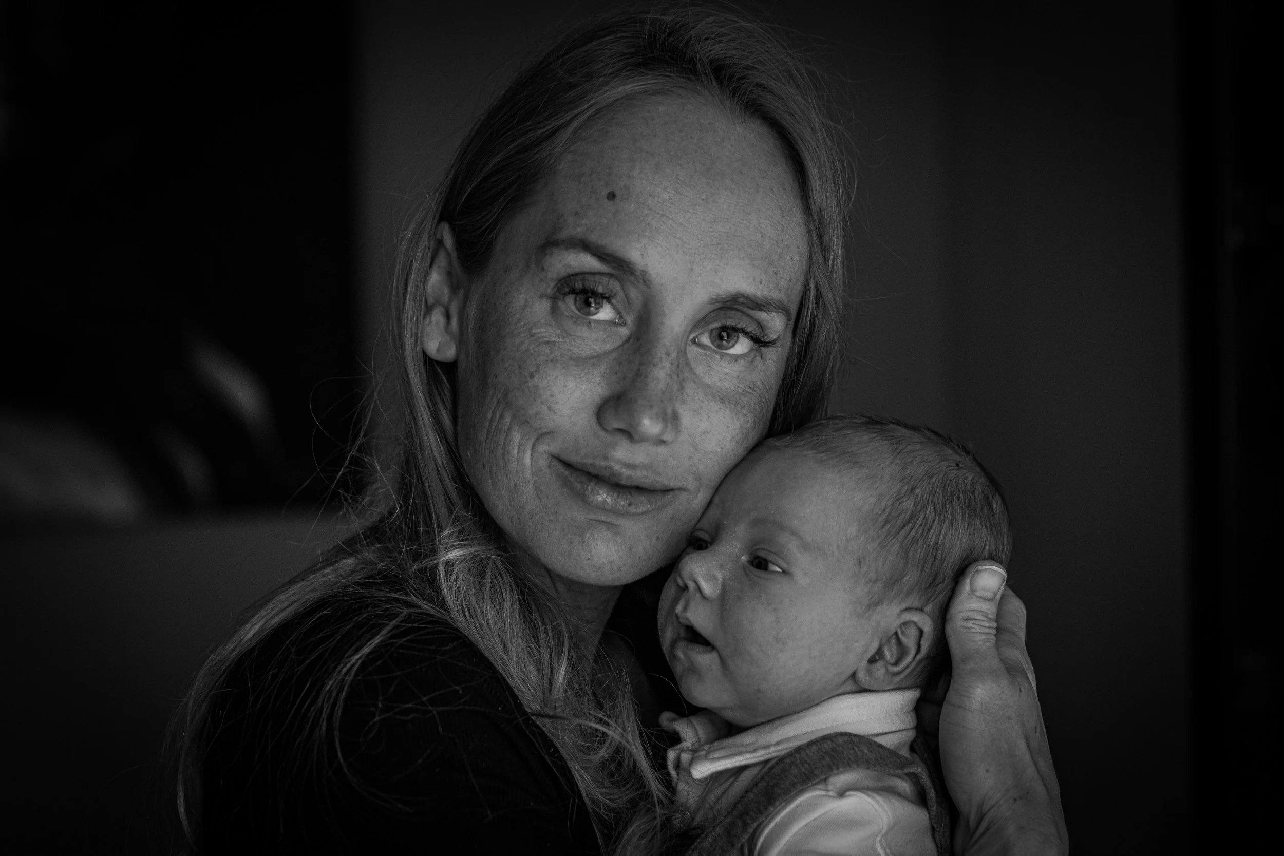 A black and white photograph of a woman holding a newborn baby closely, both showing expressions of affection and comfort.