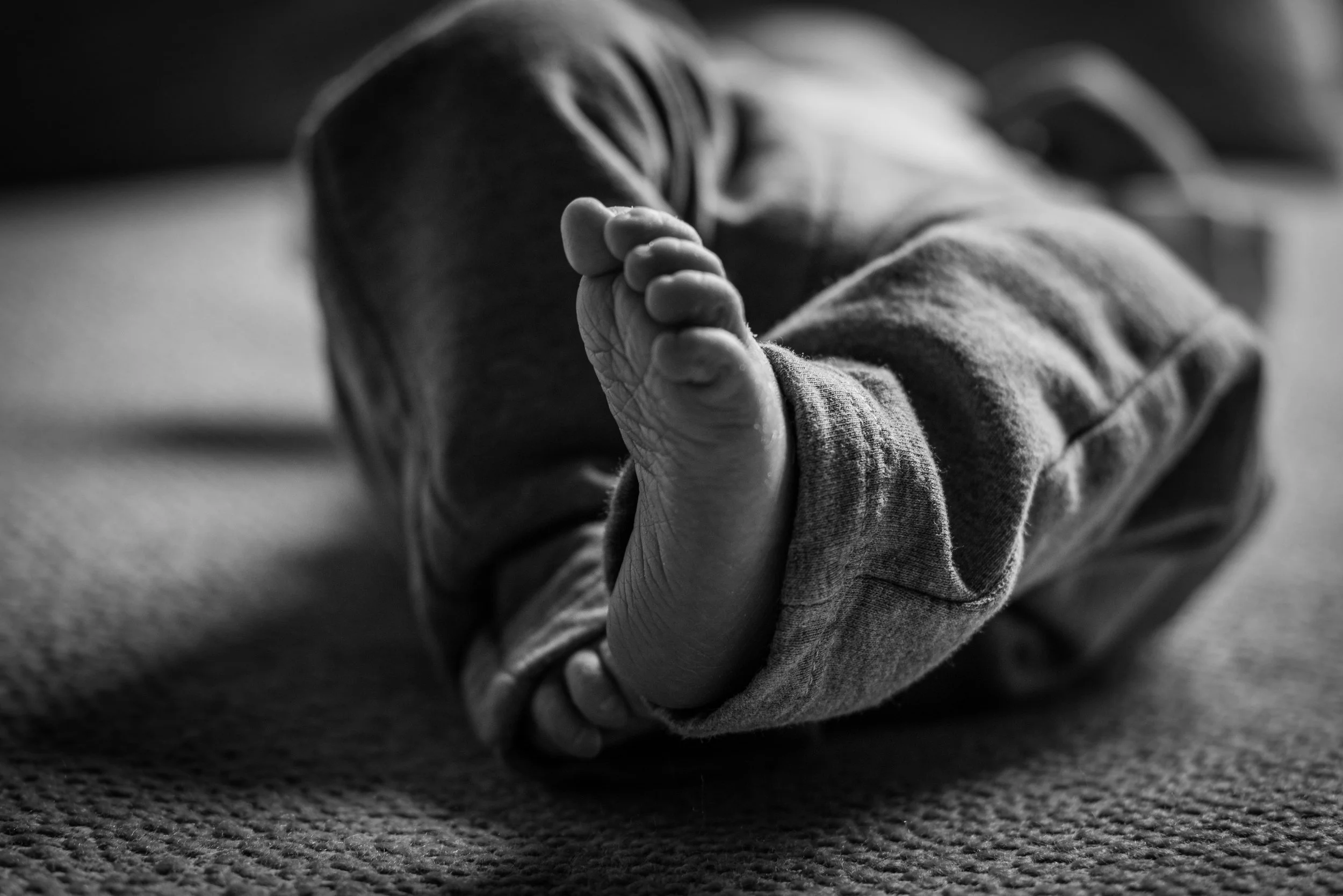 Close-up of a newborn's foot resting on a textured surface in black and white.