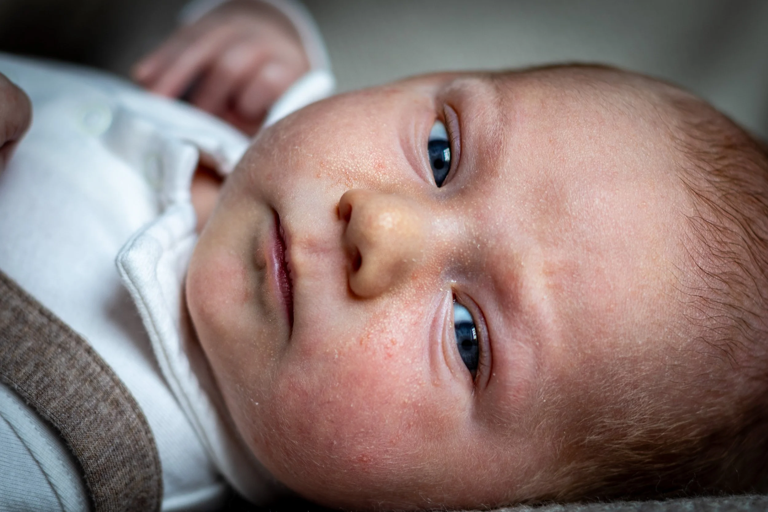 Close-up of a baby's face lying on a soft surface, with blue eyes open, light skin, and light hair.