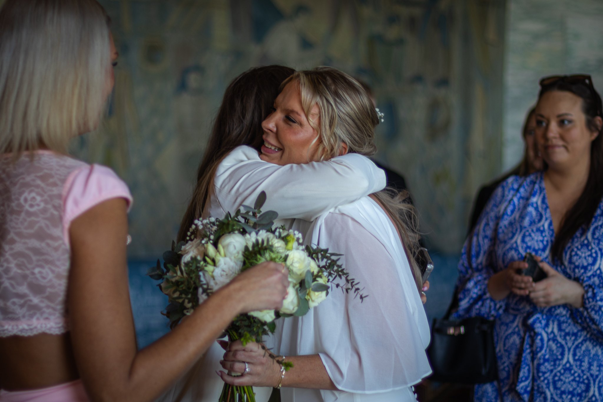 People hugging at a celebration, with one person holding a bouquet of white flowers.