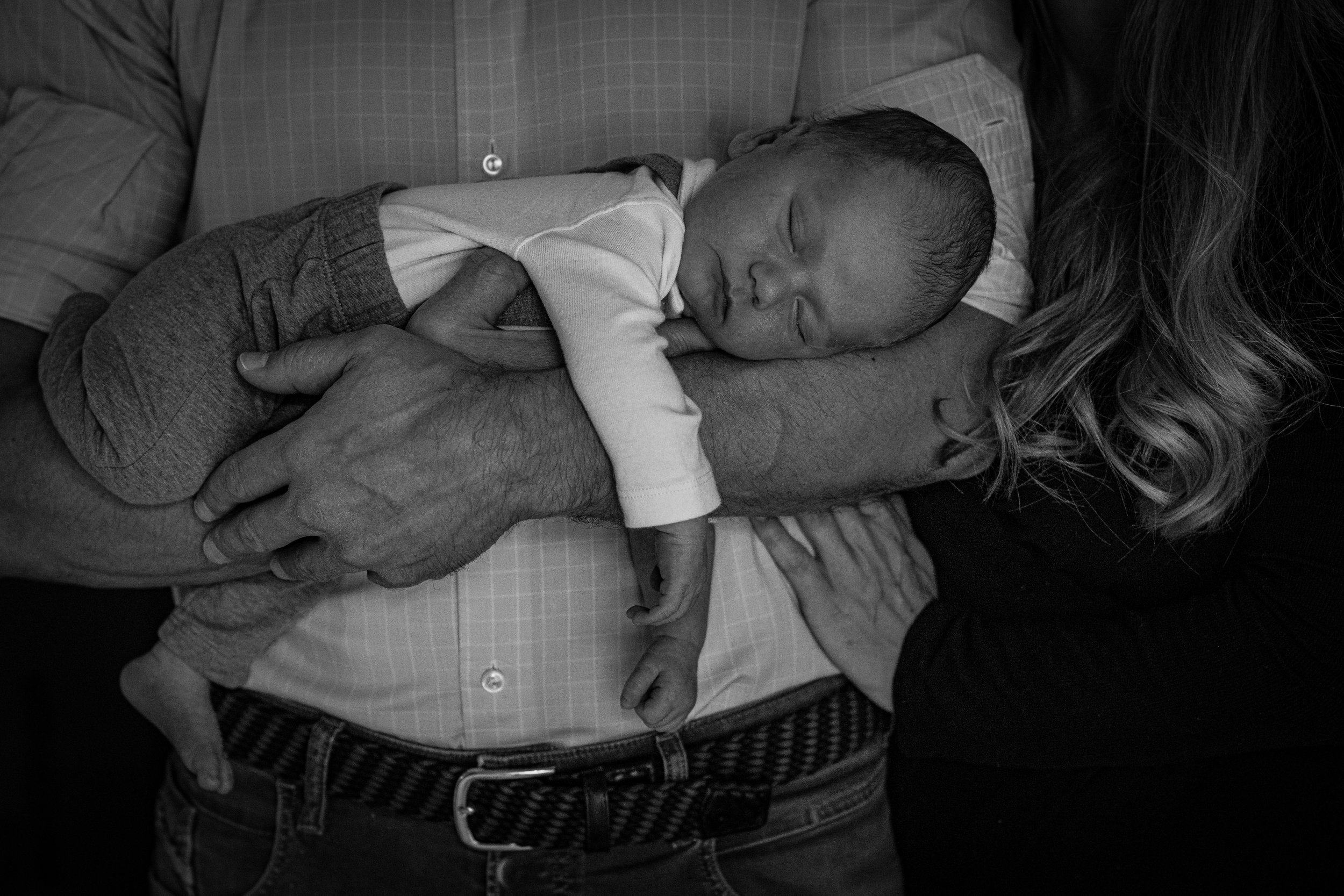 Photo of baby sleeping in father's arms, with mother nearby