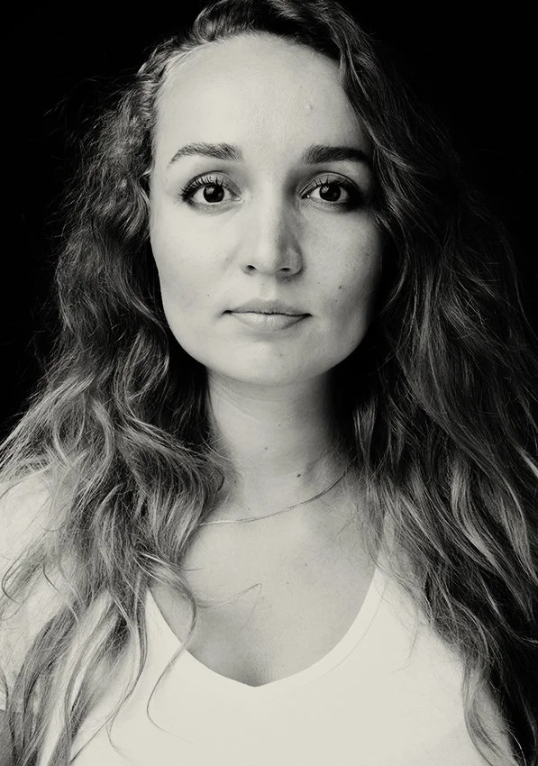 Black and white portrait of a young woman with long, wavy hair, wearing a light-colored top and a delicate necklace.