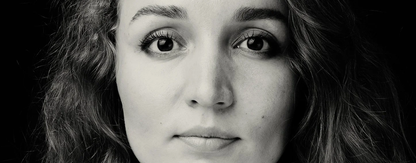 A black and white close-up of a woman’s face, showing her eyes, nose, and lips, with dark, wavy hair on her right side.