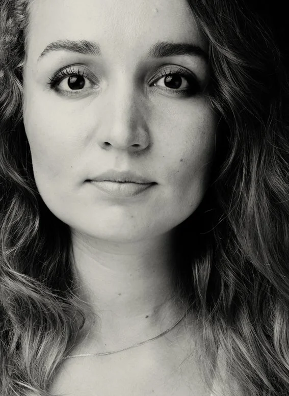 Close-up black and white portrait of a young woman with wavy hair, clear skin, and expressive eyes, looking directly at the camera.
