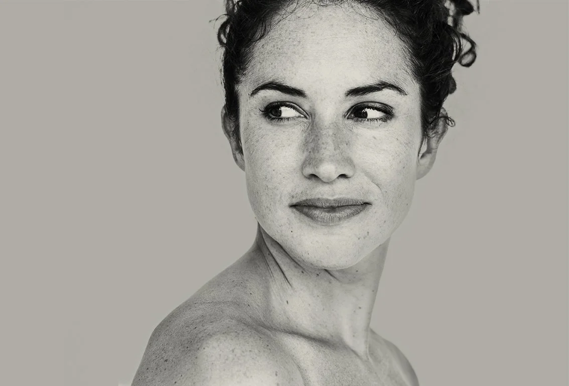 Black and white close-up portrait of a woman with short, curly hair looking to the side with a slight smile.