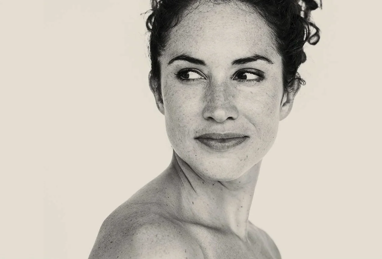 A black and white portrait of a woman with curly hair, looking to her left with a slight smile.
