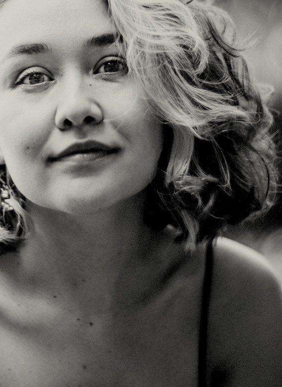 A close-up black-and-white portrait of a young woman with wavy hair, partially smiling and looking at the camera.