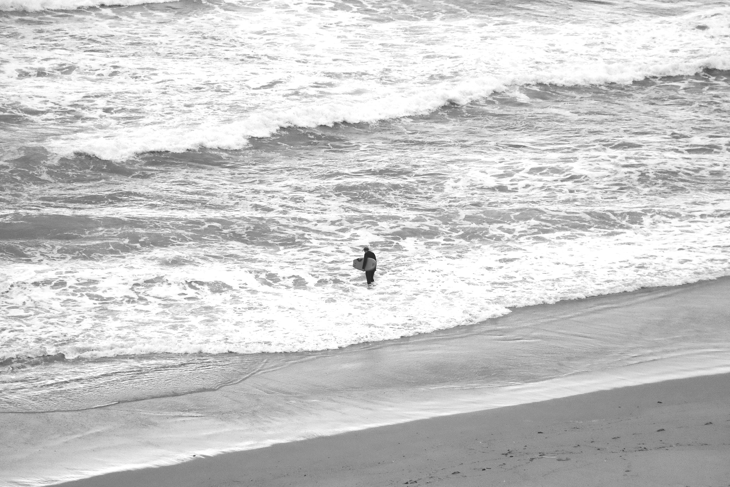 A person standing on the beach holding a surfboard, looking at the ocean waves.