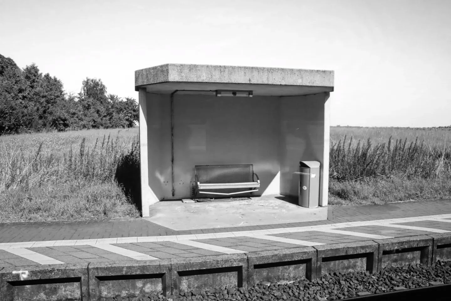 Empty bus shelter with bench and trash can on sidewalk in rural area