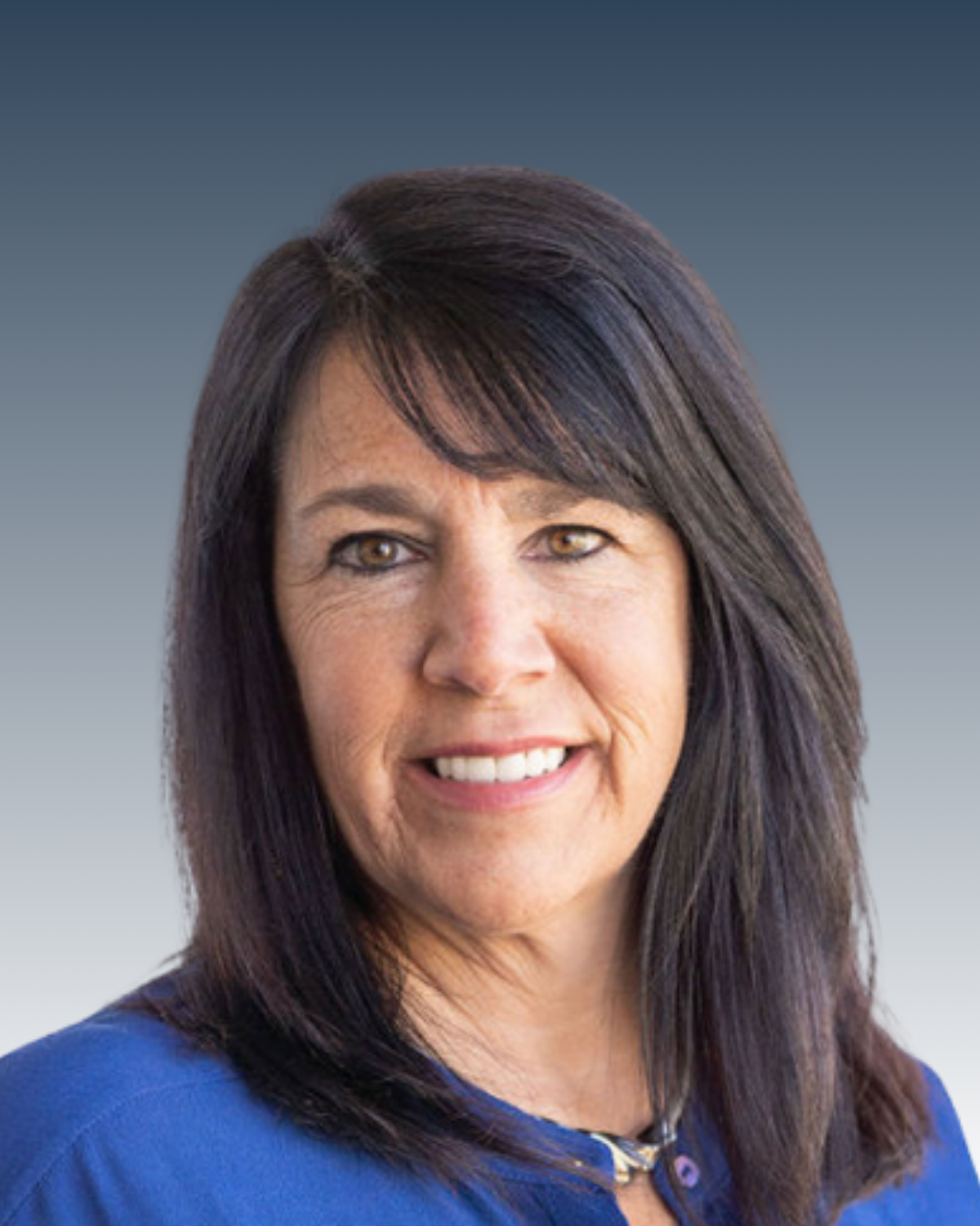 Headshot of a woman with brown hair and brown eyes, smiling, wearing a blue top against a gradient gray background.