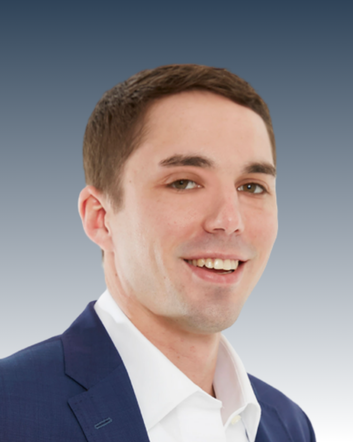 Headshot of a young man with short brown hair, wearing a dark blue suit, white shirt, smiling with teeth visible, against a gradient blue background.
