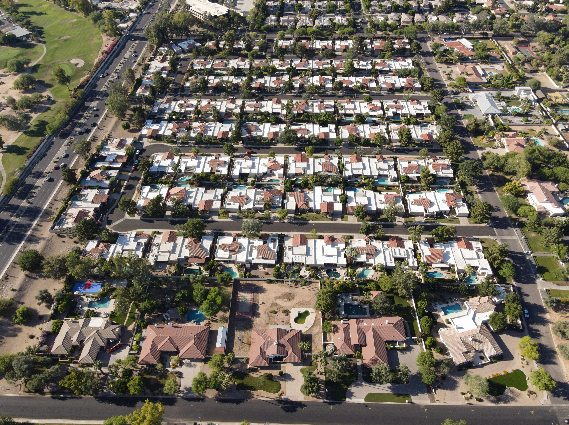 An aerial view of a residential neighborhood with houses, trees, streets, and some swimming pools.