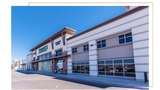 Exterior of Sprouts grocery store in a shopping center with a clear blue sky.